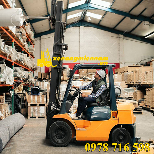 Forklift driver carefully moving stock from shelves while working on the floor of a large carpet warehouse